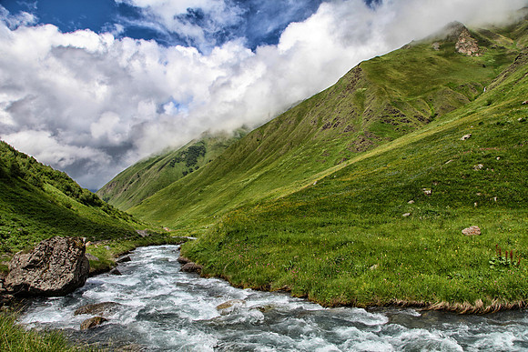 A river stream flows down the Caucasus Mountains with storm clouds in the air
